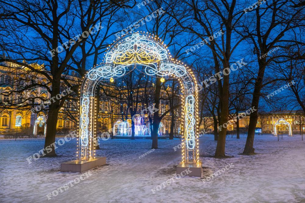 На фотографии изображены световые арки, установленные около Эрмитажа на Дворцовой площади в Санкт-Петербурге. Украшенные гирляндами арки создают сказочную атмосферу зимнего вечера. Заснеженная земля и яркий свет иллюминации подчёркивают торжественность и красоту места. Эрмитаж, освещённый в ночи, дополняет ощущение праздника и уюта, делая это место любимым для прогулок в новогодний период.